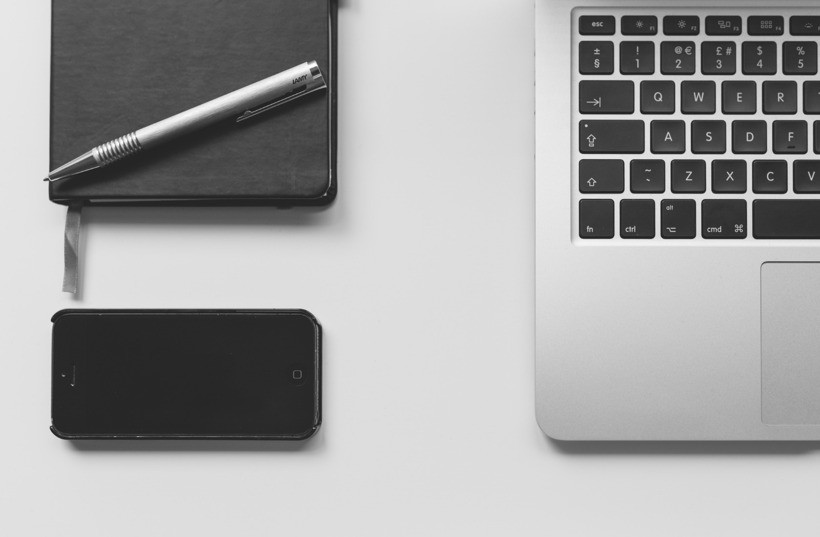 A minimal desk setup with a notebook, pen, phone, and laptop